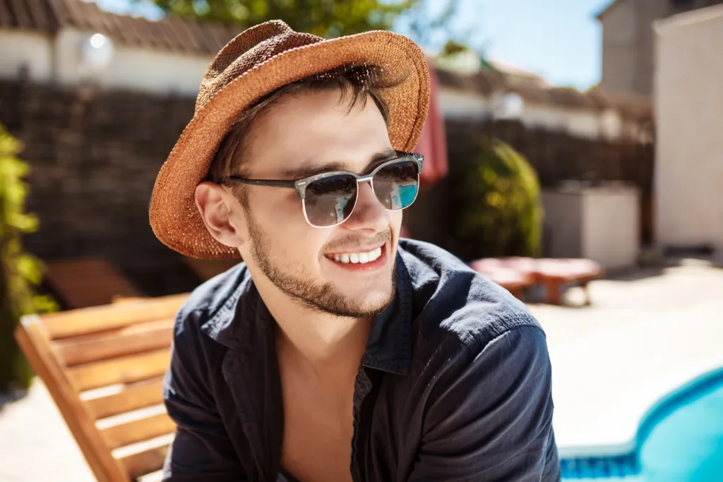 man sunglasses hat smiling sitting near swimming pool